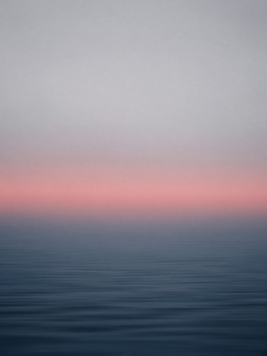 Abstract photograph of fog, a thin rose band of light, and dark water.